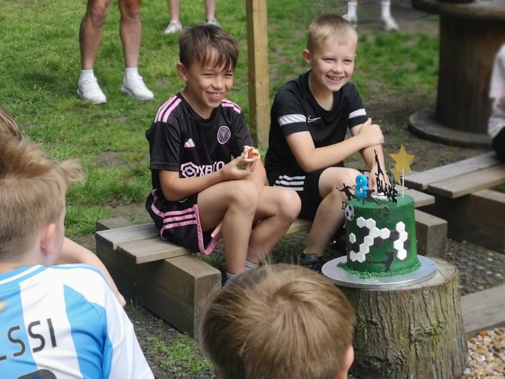 Children gathered around a campfire enjoying birthday cake, with glowing flames, happy faces, and a festive outdoor atmosphere
