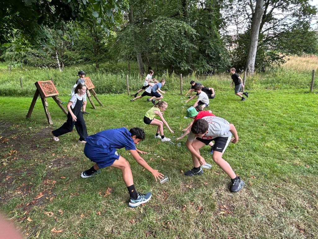 Children playing high-energy outdoor games at a birthday party, running, laughing, and participating in team challenges on a grassy field.
