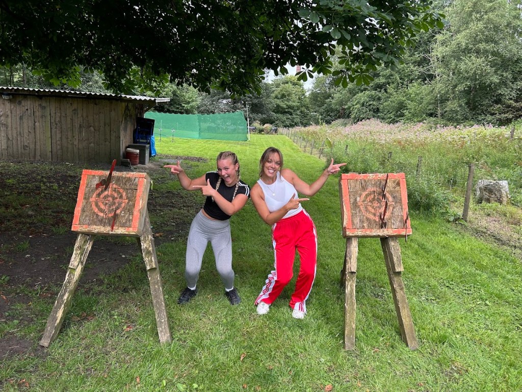 Two smiling participants posing on our grassy tomahawk range at Wood-Sage Outdoor, each pointing proudly at their target