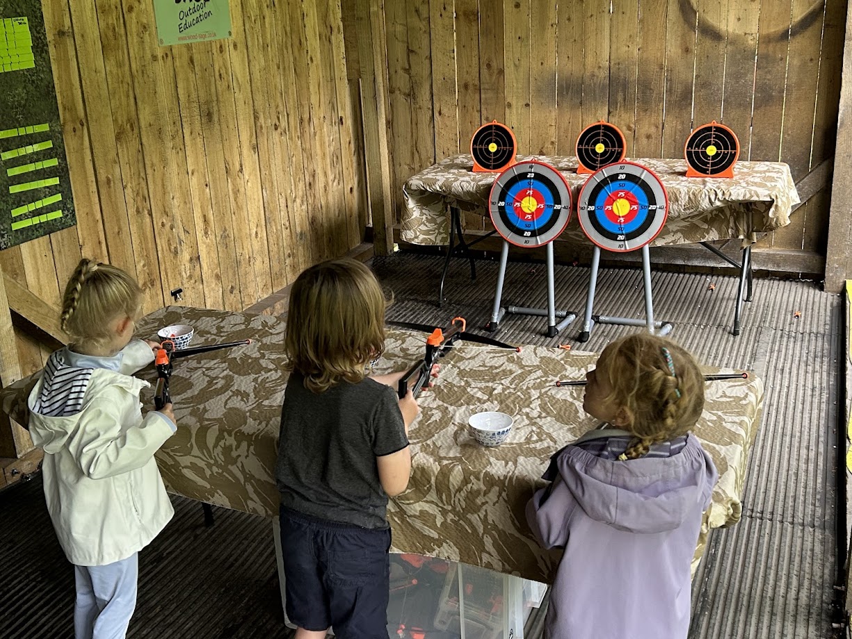 Child aiming a toy crossbow at a colourful target during a supervised kids' activity session, with sucker darts.