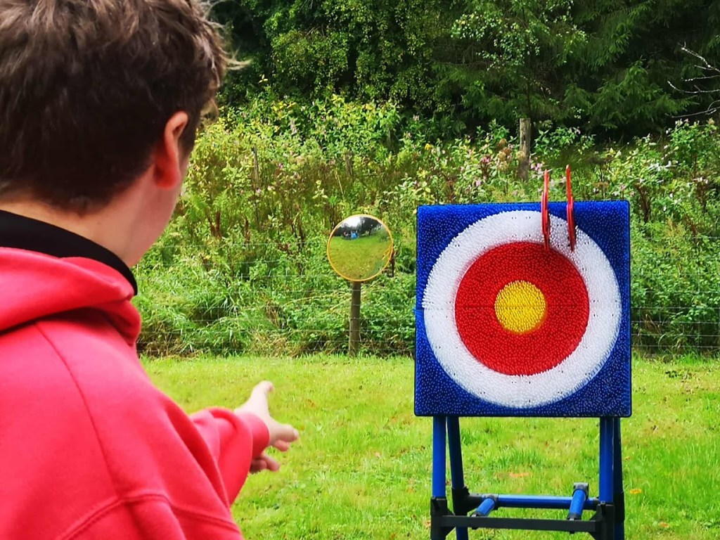 A young person carefully throwing a soft axe at a target outdoors, supervised for safety, as part of a fun and confidence-building activity